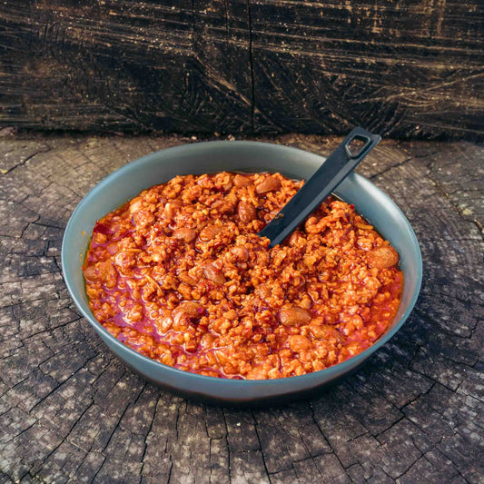 Chili alla Texana Outfood con fagioli e paprika affumicata in ciotola grigia con cucchiaio nero, su fondo di legno.
