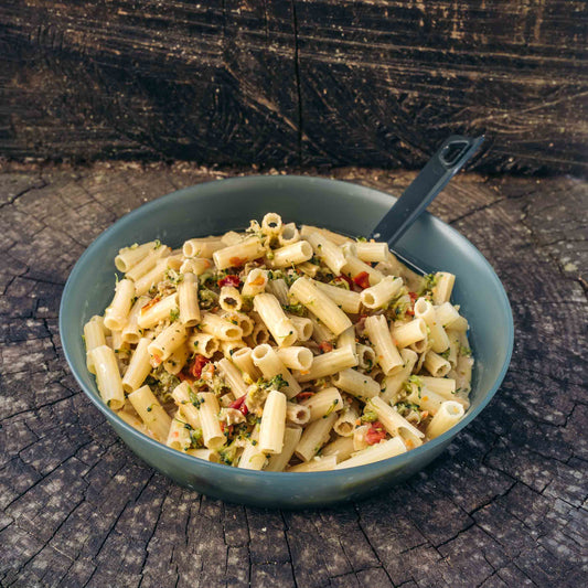 Pasta ai broccoli e pomodoro secco Outfood in una ciotola grigia con una paletta nera su un tronco di legno.