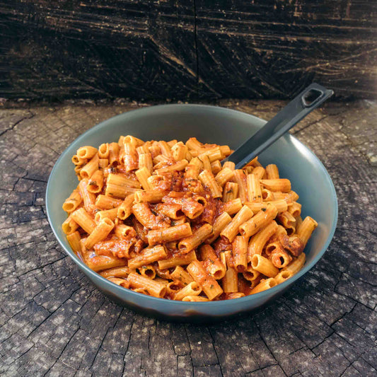 Pasta alla Puttanesca Outfood in una ciotola grigia con cucchiaio, su un tronco d'albero.