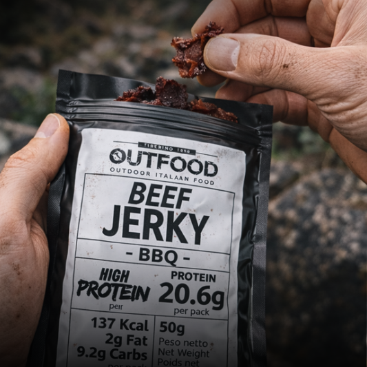 Mani tengono una busta nera opaca di Beef Jerky Outfood BBQ da 50g e un pezzo di carne essiccata.