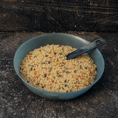 Couscous con verdure Outfood in ciotola grigio-blu con cucchiaio nero su sfondo di legno scuro.