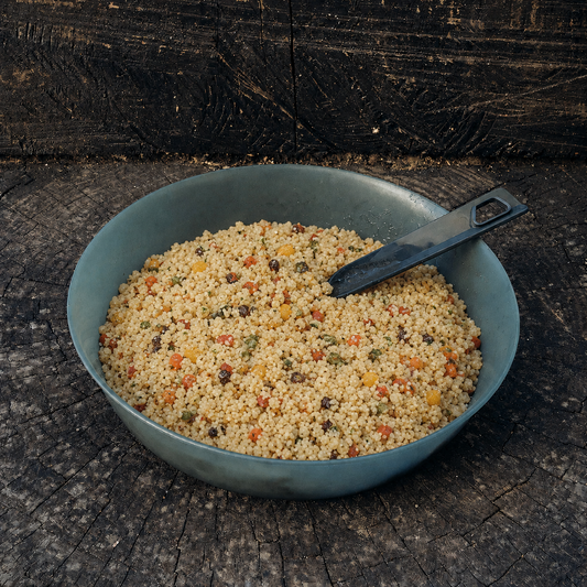 Couscous con verdure Outfood in ciotola grigio-blu con cucchiaio nero su sfondo di legno scuro.
