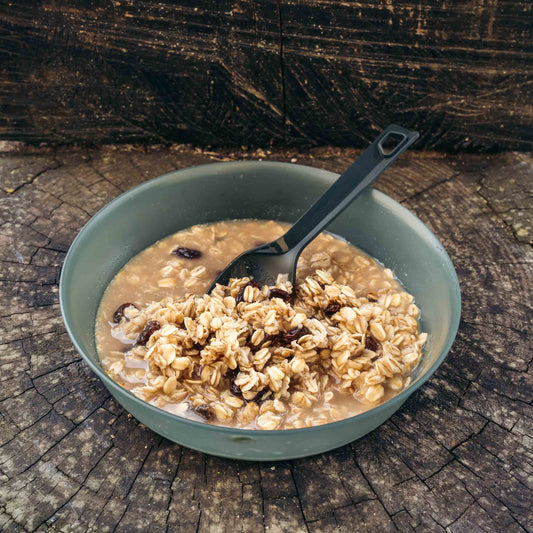 Porridge di avena con uvetta e mandorle in ciotola verde scuro con cucchiaio nero, su superficie di legno.