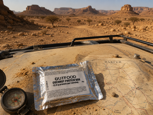 Barretta proteica Outfood al cocco da 45g in confezione argentata su mappa antica, bussola e tetto di veicolo nel deserto.