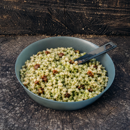Risotto ai broccoli e pomodoro secco Outfood in ciotola grigia con cucchiaio nero su tronco di legno scuro.
