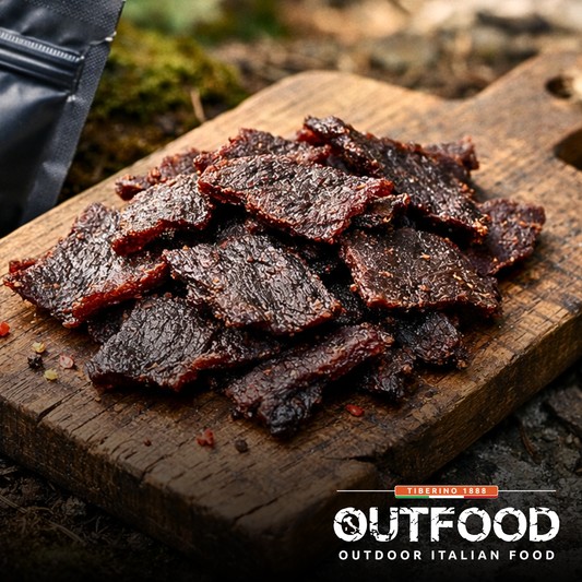 Fette di manzo essiccato Outfood Classico e BBQ su tagliere di legno scuro, con confezione nera sullo sfondo.